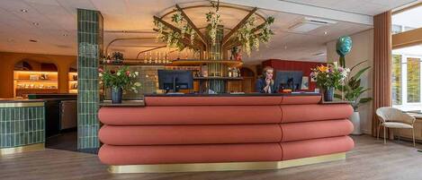 A reception area with a modern design, featuring a curved reception desk, a bar area, and a large decorative plant.