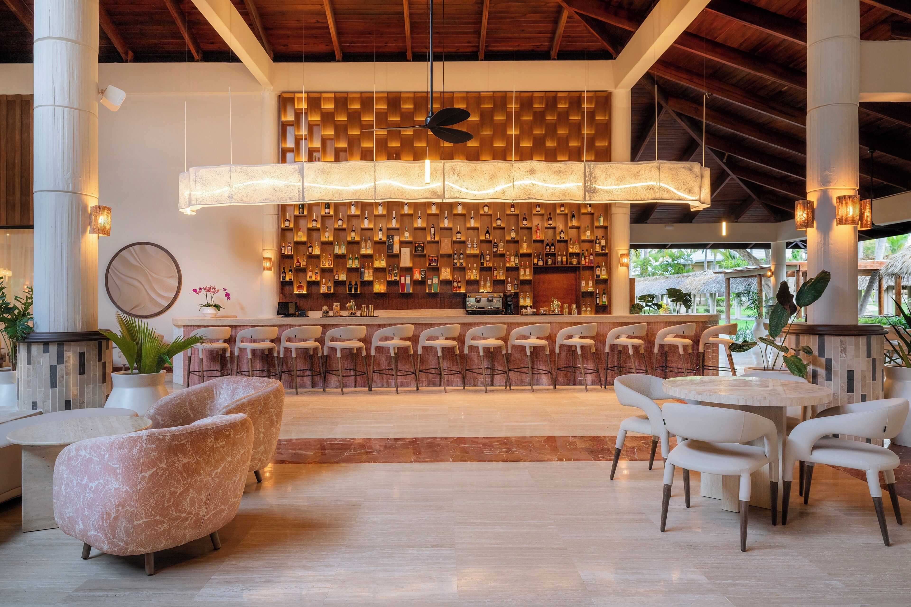 A bar area with a wall of bottles, bar stools, and a hanging light fixture.