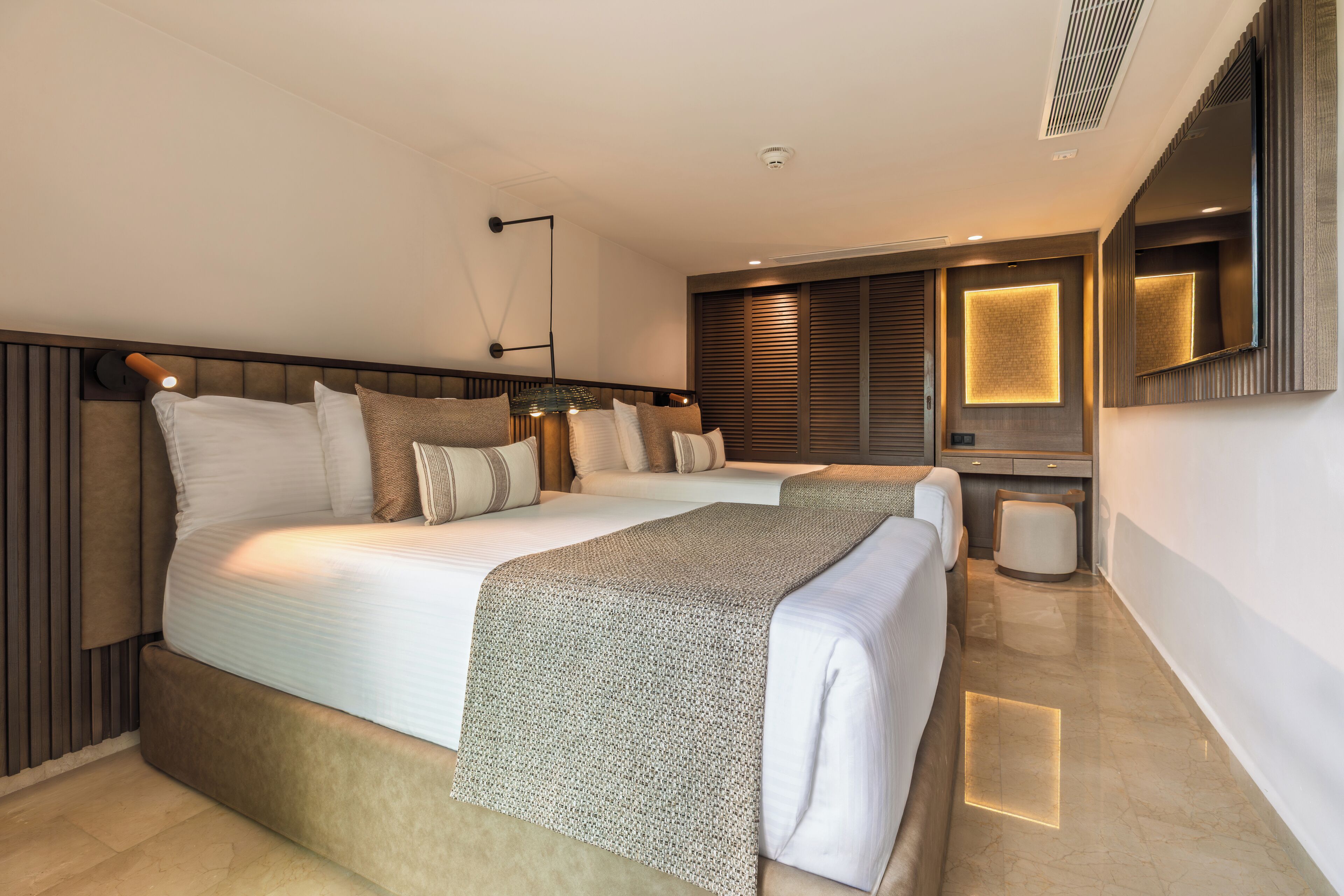 Une chambre d’hôtel moderne, dotée d’un grand lit, d’une table de chevet, d’un miroir et d’un luminaire fixé au mur.