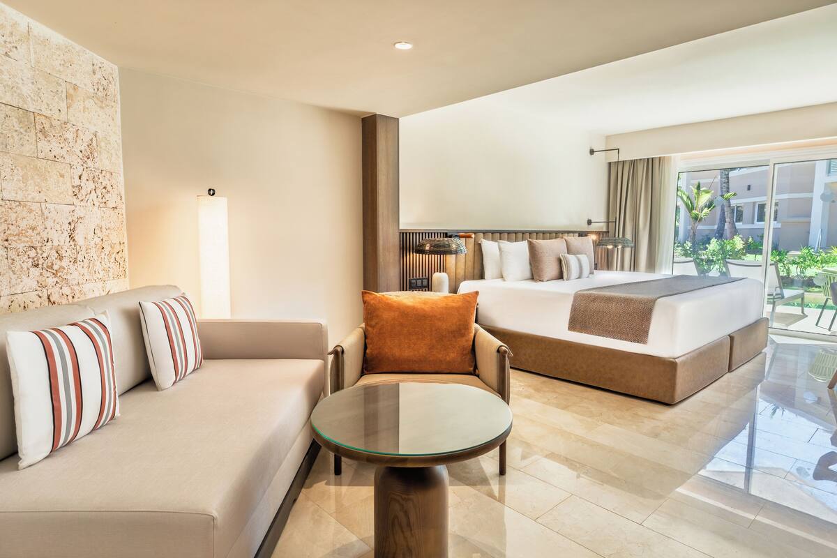 Une chambre d’hôtel moderne avec un canapé, un lit, une table en verre et une vue sur l’extérieur.