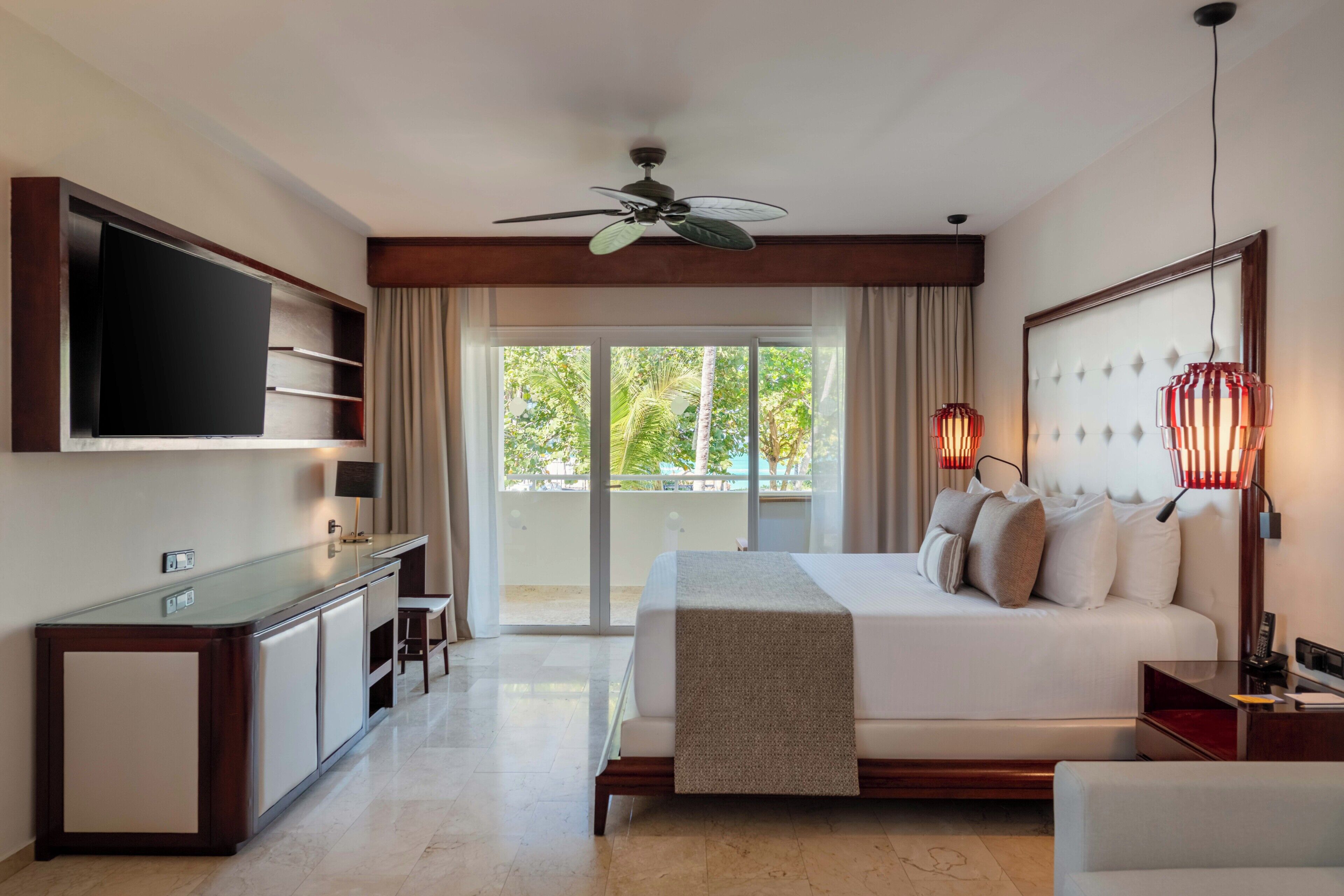 A hotel room with a bed, a TV, a desk, and a balcony with a view.