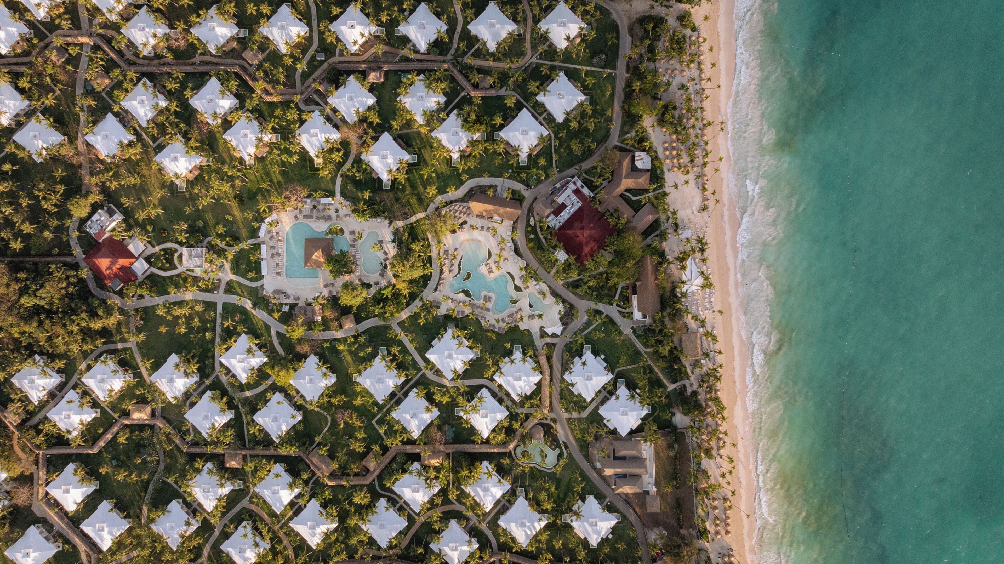 An aerial view of a resort with multiple bungalow-style accommodations, a central pool area, and a beach.