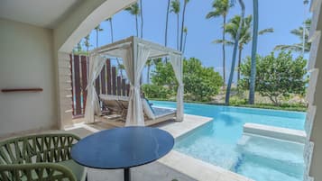 Zona de piscina con área de estar cubierta, una mesa y vistas a la piscina y palmeras.