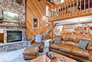 A spacious living area with a stone fireplace, leather sofas, and a wooden staircase.