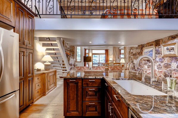 A spacious kitchen with wooden cabinets, a marble countertop, and a large sink.