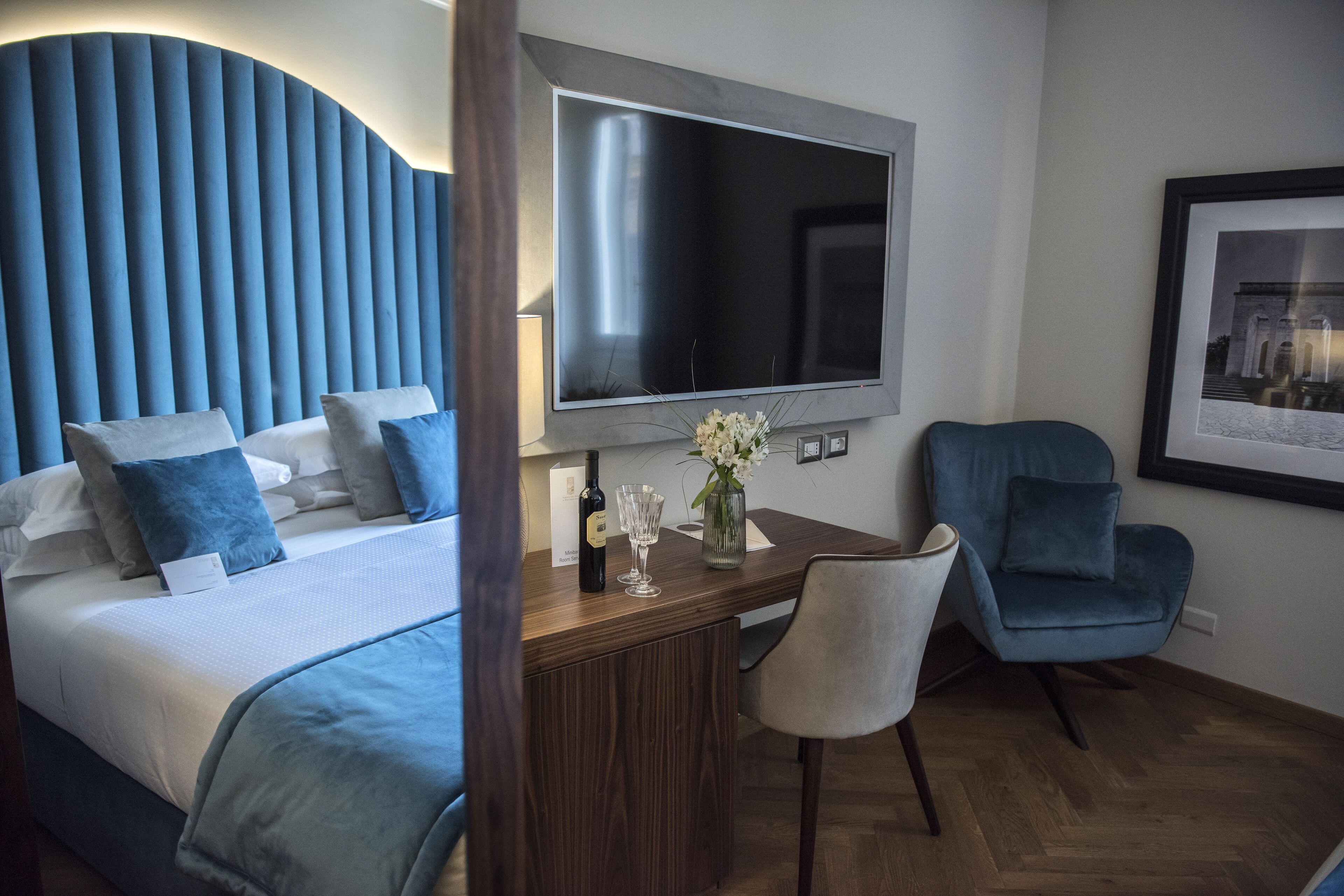 Une chambre d’hôtel avec un lit, un bureau avec une télévision, une chaise et un tableau encadré au mur.