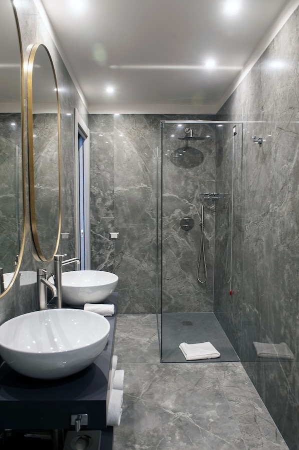 Un baño moderno con un espejo grande, dos lavamanos, una ducha con cerramiento de vidrio y paredes de mármol.