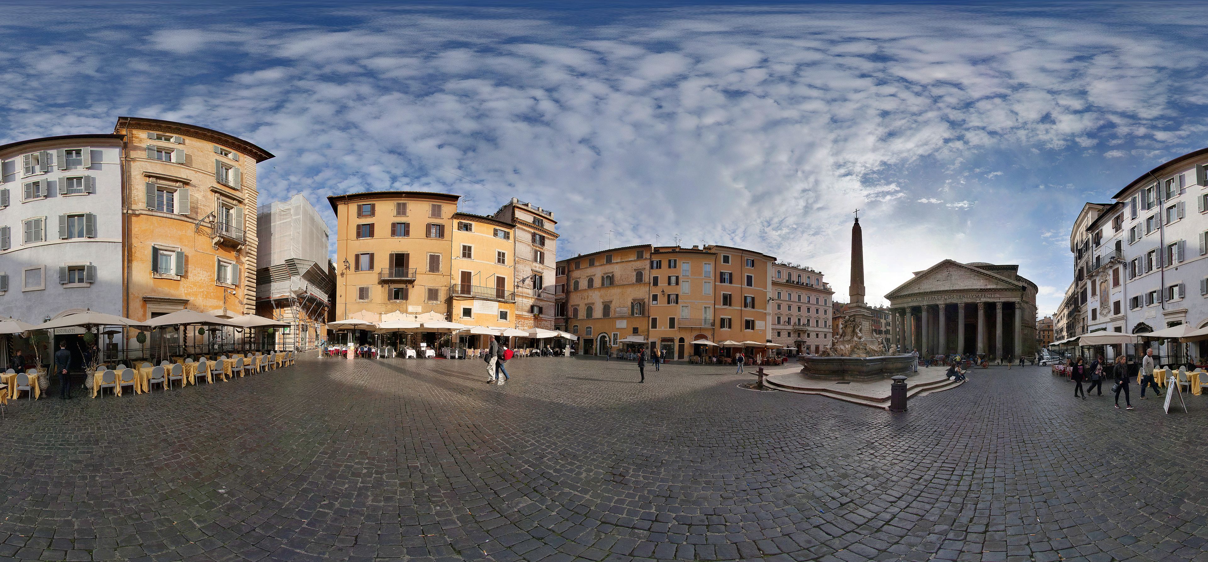 A cobblestone square with historic buildings, outdoor seating, and a fountain.