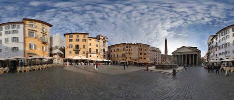 A cobblestone square with historic buildings, outdoor seating, and a fountain.