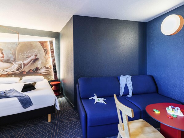 Una habitación de hotel con una cama, un sofá azul, una mesita y una pared decorada con un cuadro.
