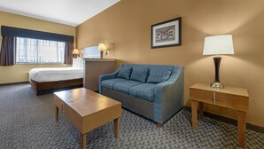 A hotel room with a bed, a sofa, a desk, and a lamp.