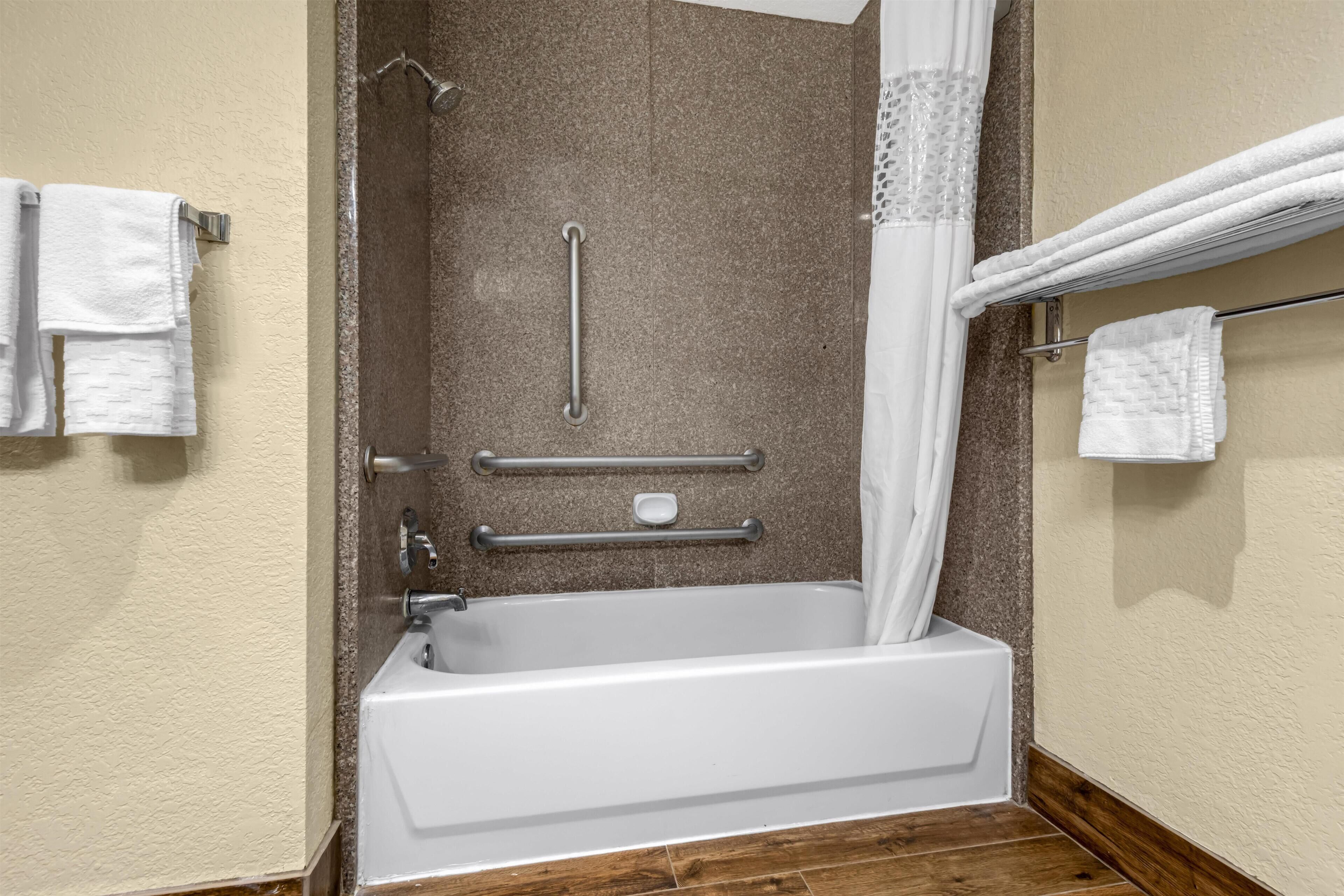 A bathroom with a bathtub, a shower with a grab bar, and white towels on a rack.