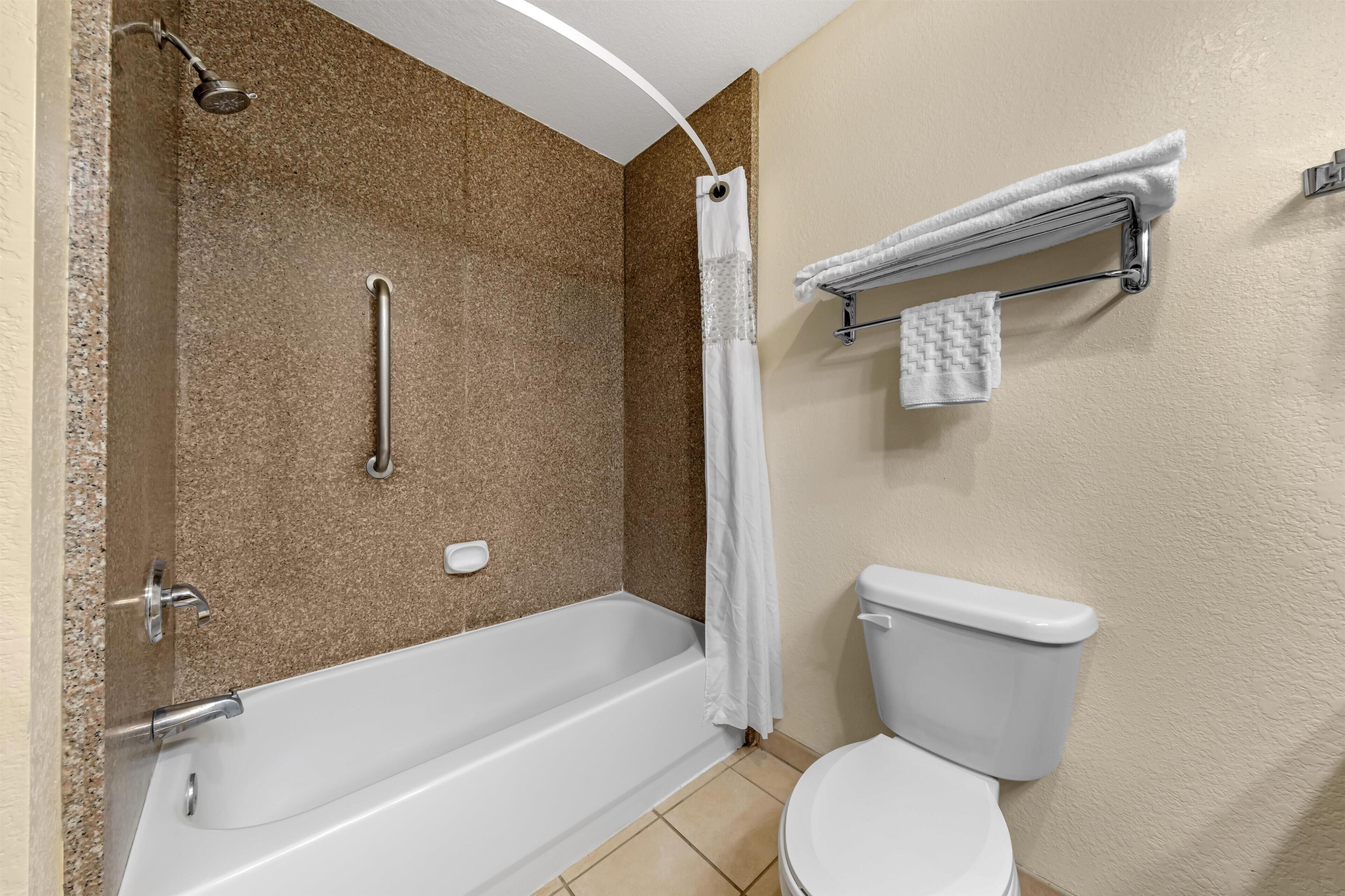Ein Badezimmer mit Badewanne, Toilette und Dusche inklusive Handbrause sowie einer Haltestange.