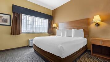 A hotel room with a large bed, two bedside lamps, a window with curtains, and a framed picture on the wall.