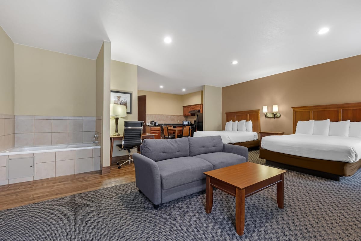 Ein Hotelzimmer mit Sofa, Bett, Schreibtisch, Stuhl, Lampe und einem Badezimmer mit Badewanne.