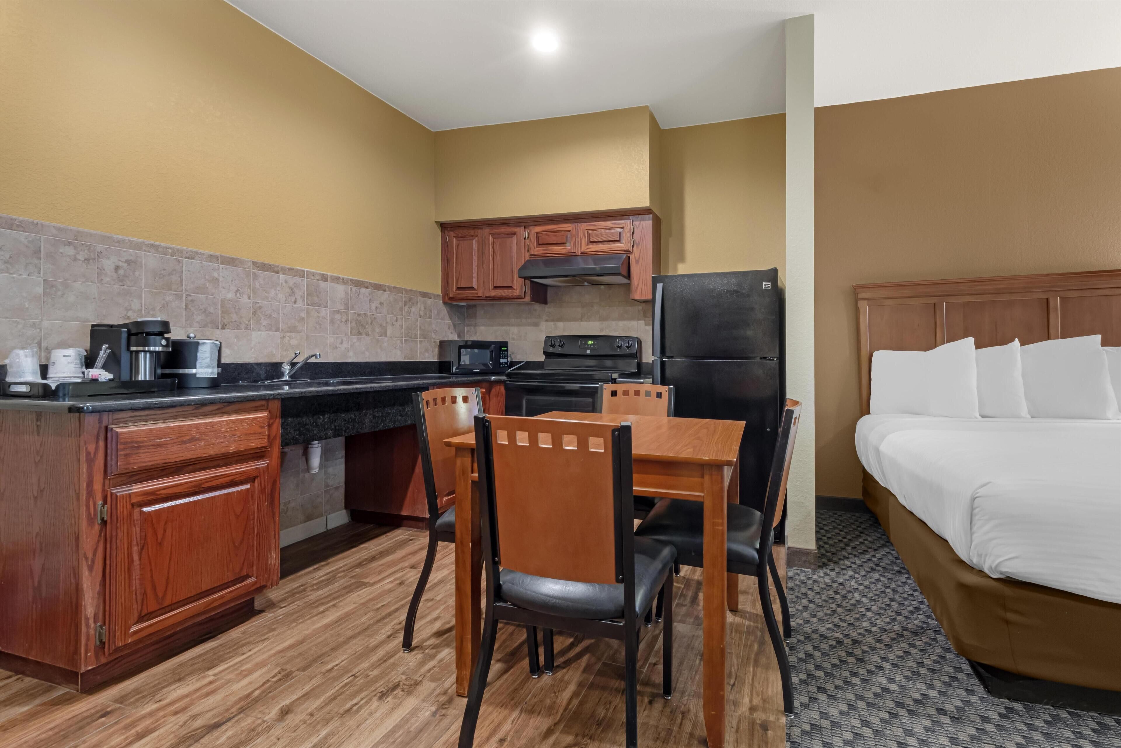 A compact hotel room with a kitchenette, wooden furniture, and a bed with white bedding.