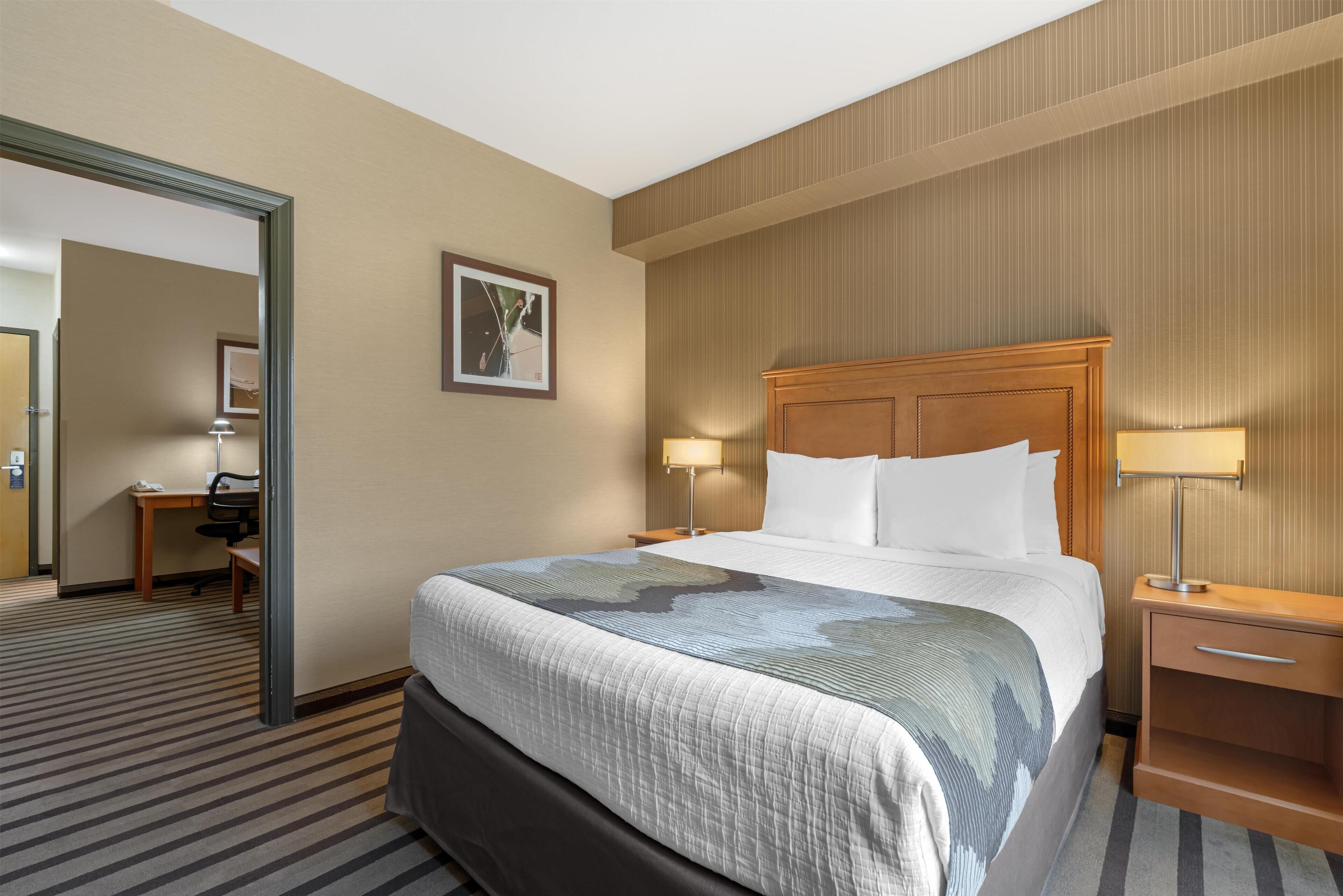 A hotel room with a large bed, bedside tables with lamps, a desk with a chair, and a framed picture on the wall.