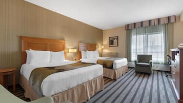 A hotel room with two beds, a chair, a desk, and a large window with curtains.