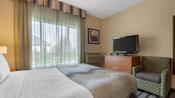 Habitació d'hotel amb un llit, una televisió, una cadira i una finestra amb cortines.