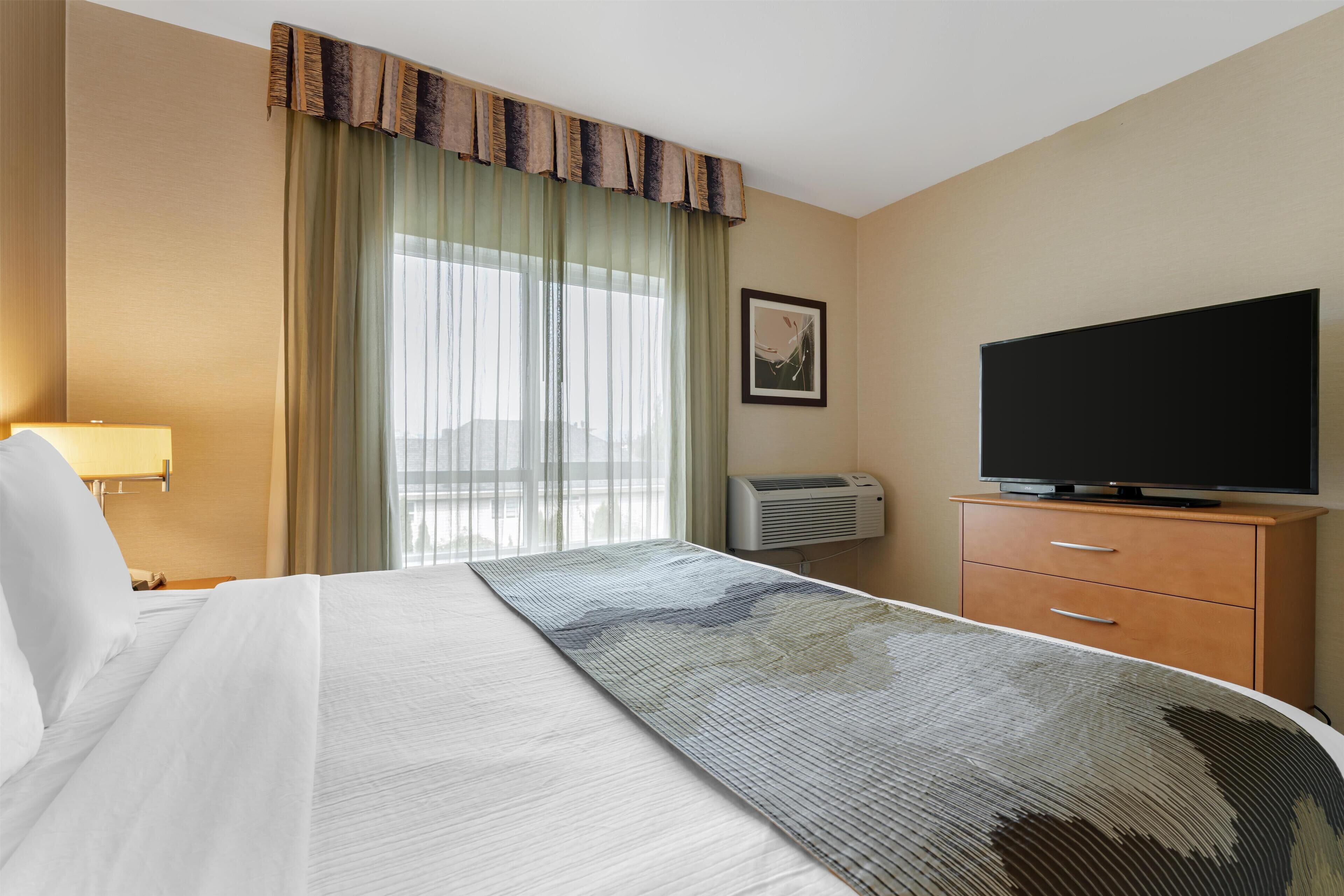 Een hotelkamer met een bed, een televisie, een bureau en een raam met gordijnen.