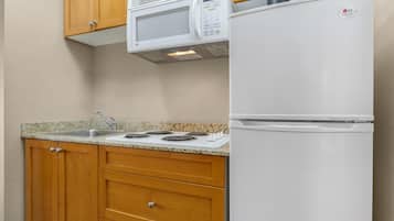 A kitchen with wooden cabinets, a granite countertop, a microwave, a refrigerator, and a stove.