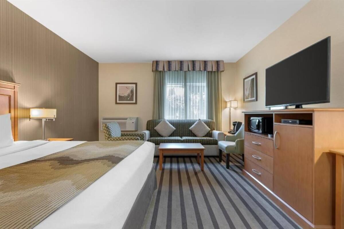 A hotel room with a bed, a sofa, a TV, a desk, and a cabinet.