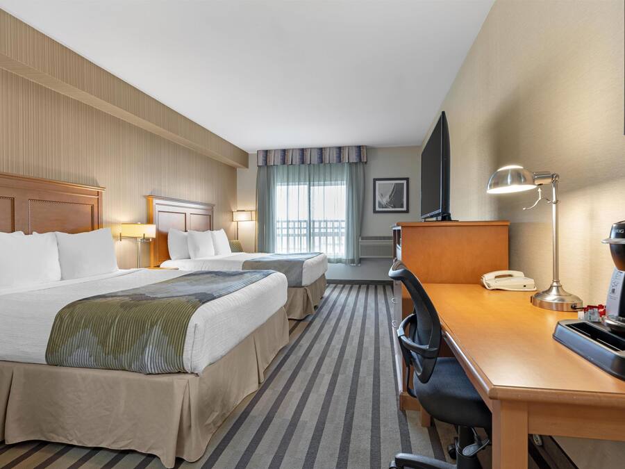 Une chambre d’hôtel avec deux lits, un bureau doté d’un téléphone et d’une machine à café, une chaise et un téléviseur.