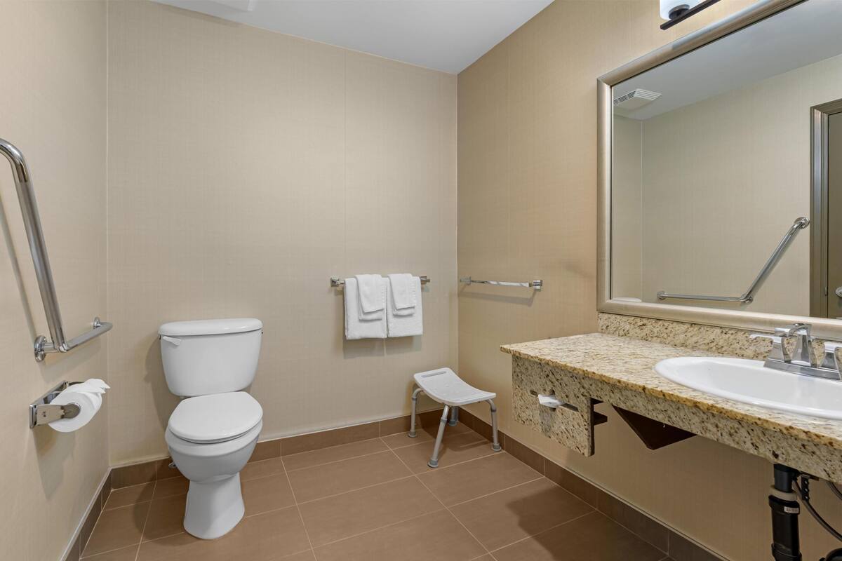 A bathroom with a toilet, a sink, a mirror, and a small step stool.