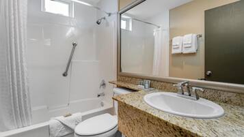 Un baño moderno con ducha de vidrio, inodoro blanco y lavamanos sobre encimera de granito.