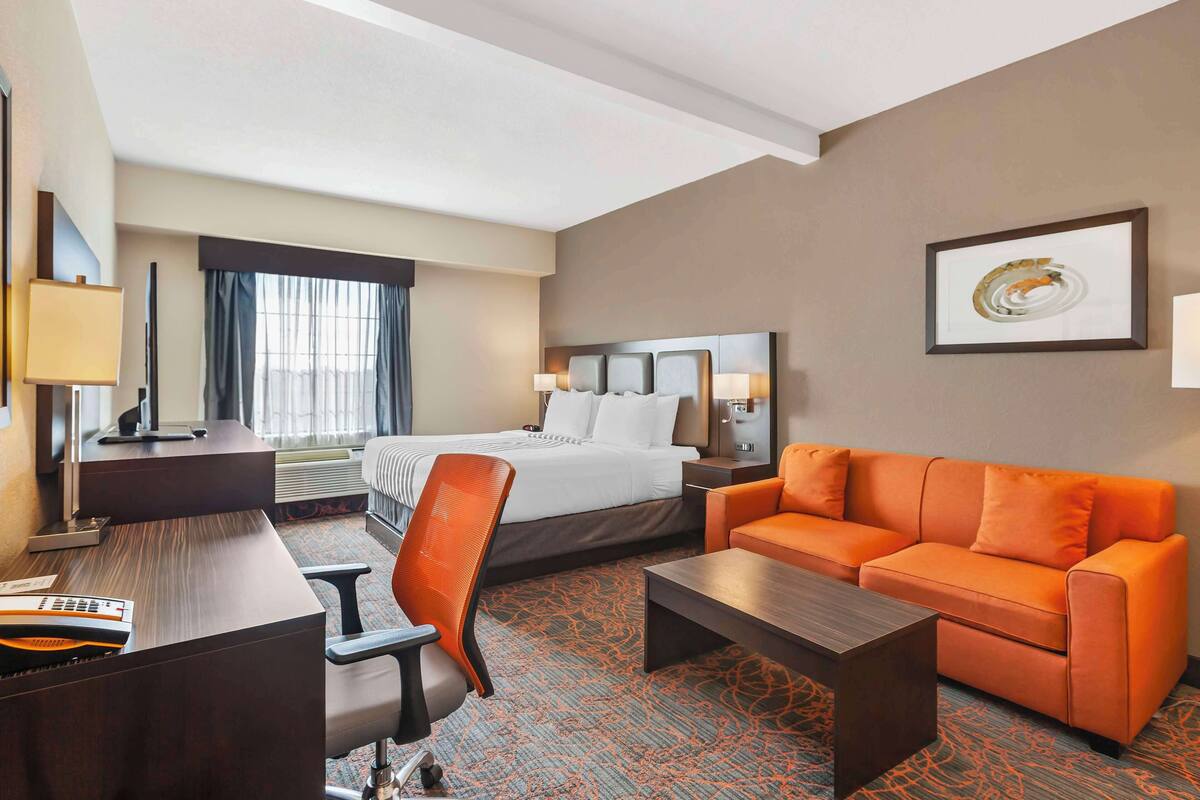 A hotel room with a bed, orange sofa, desk, chair, and a coffee table.