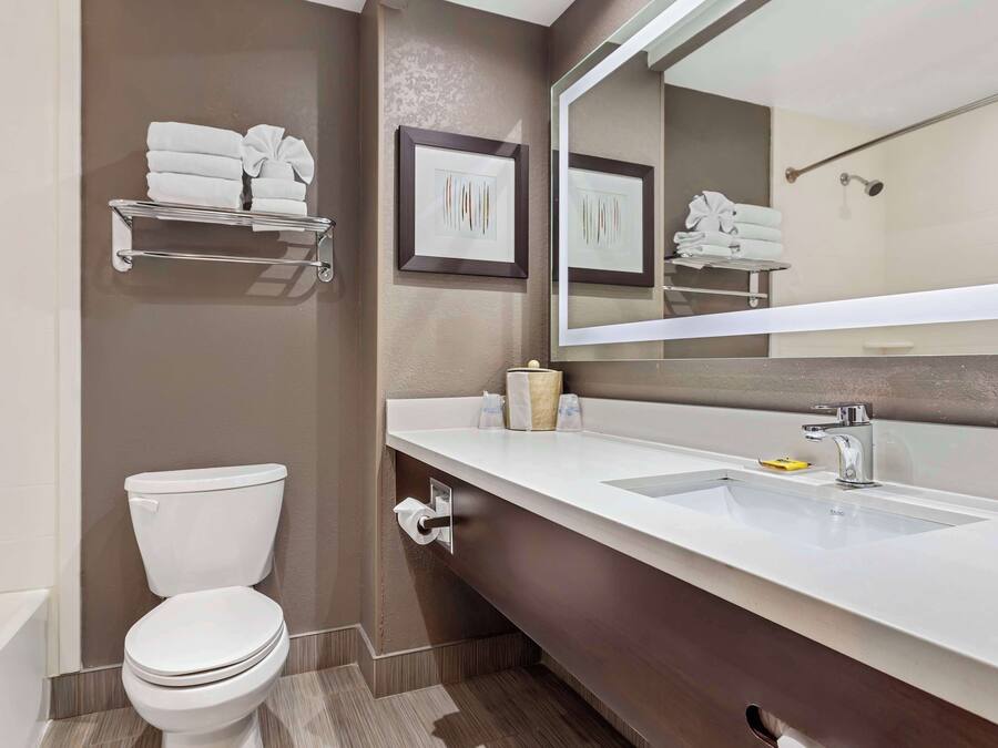 Un baño moderno con inodoro, lavamanos, espejo y toallero.