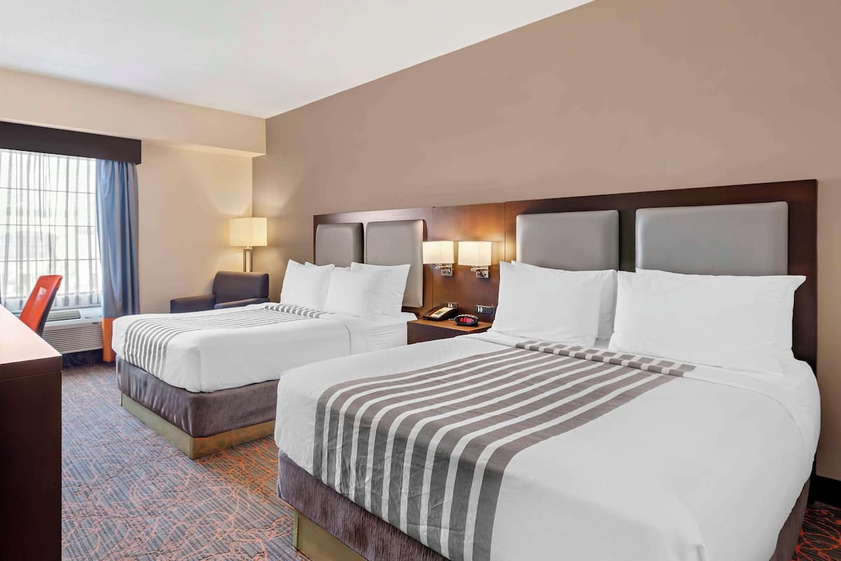 A hotel room with two beds, a desk, a chair, a lamp, and a window with curtains.