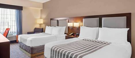 A hotel room with two beds, a desk, a chair, a lamp, and a window with curtains.