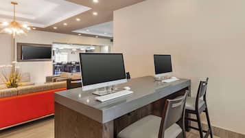 Un moderno vestíbulo de hotel con un mostrador de recepción, dos monitores de ordenador, un televisor plano grande y una zona de estar con una pared de acento roja.