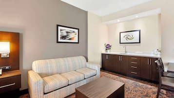 Quarto de hotel com sofá, mesa de centro, escrivaninha com luminária, pia e armários.