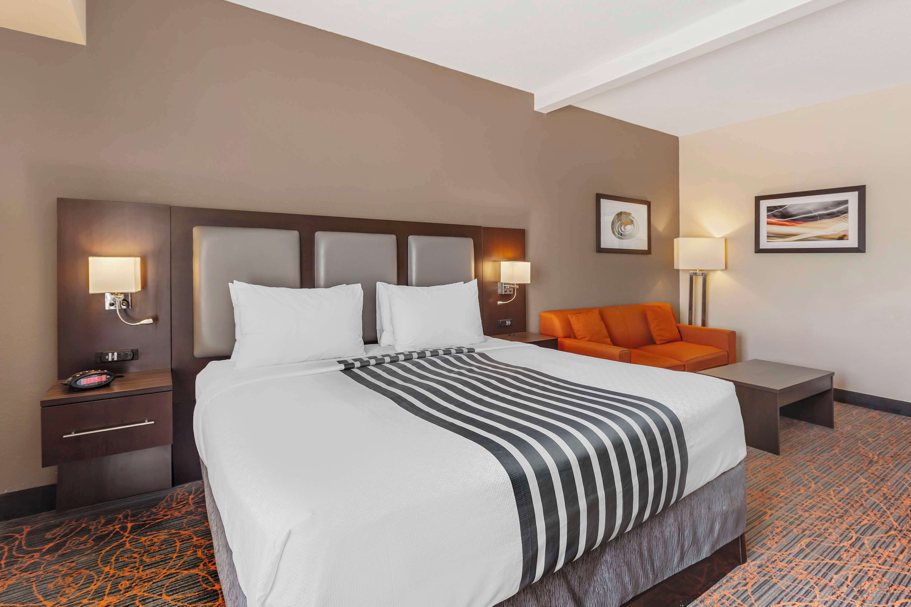 A hotel room with a large bed, two bedside tables with lamps, an orange sofa, and a small table.