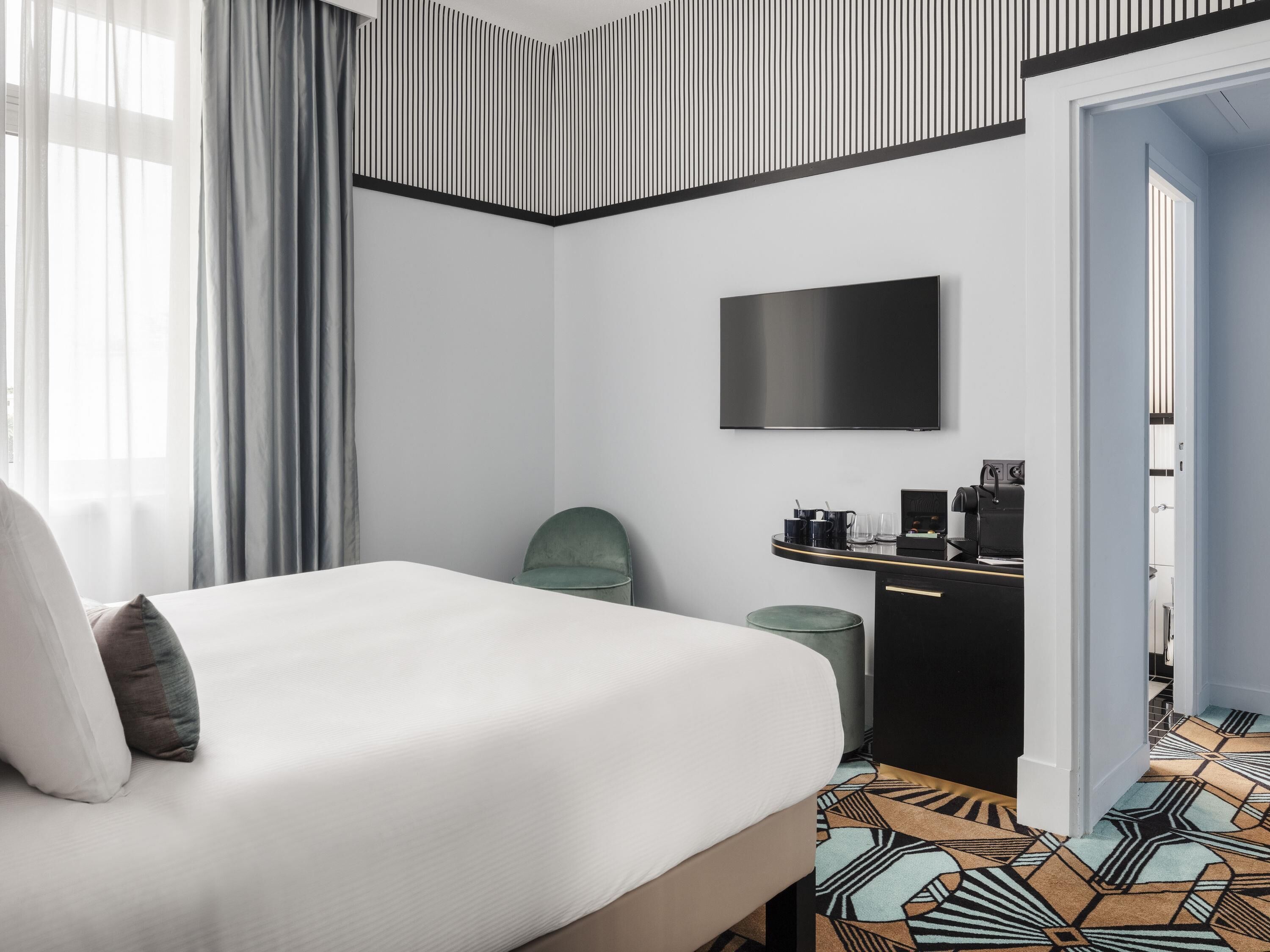 Une chambre d’hôtel avec un lit, une télévision, un bureau avec une machine à café et un sol à motifs.
