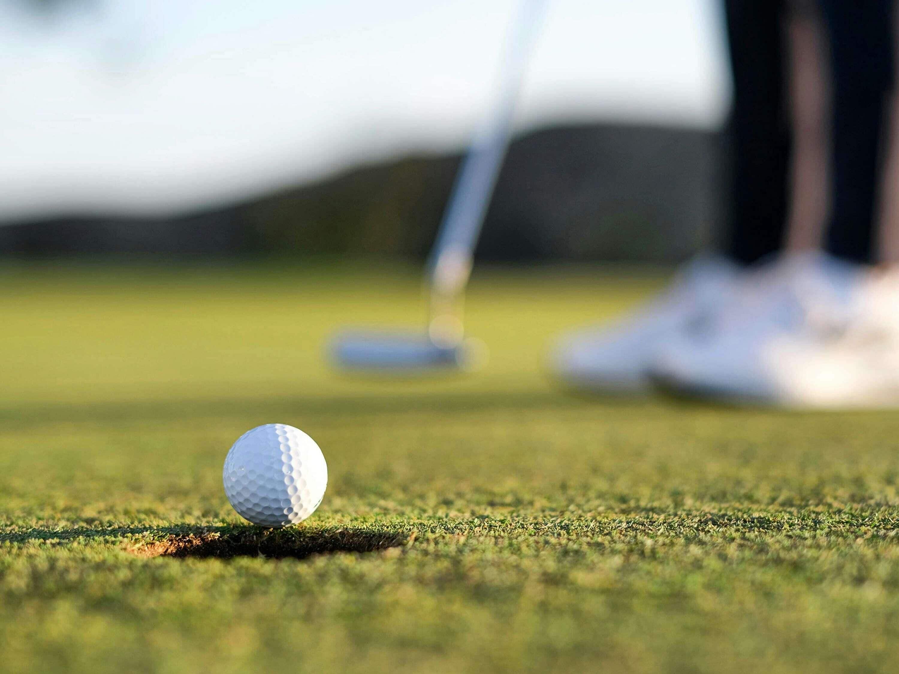 A golf ball on a green with a golf club in the background.