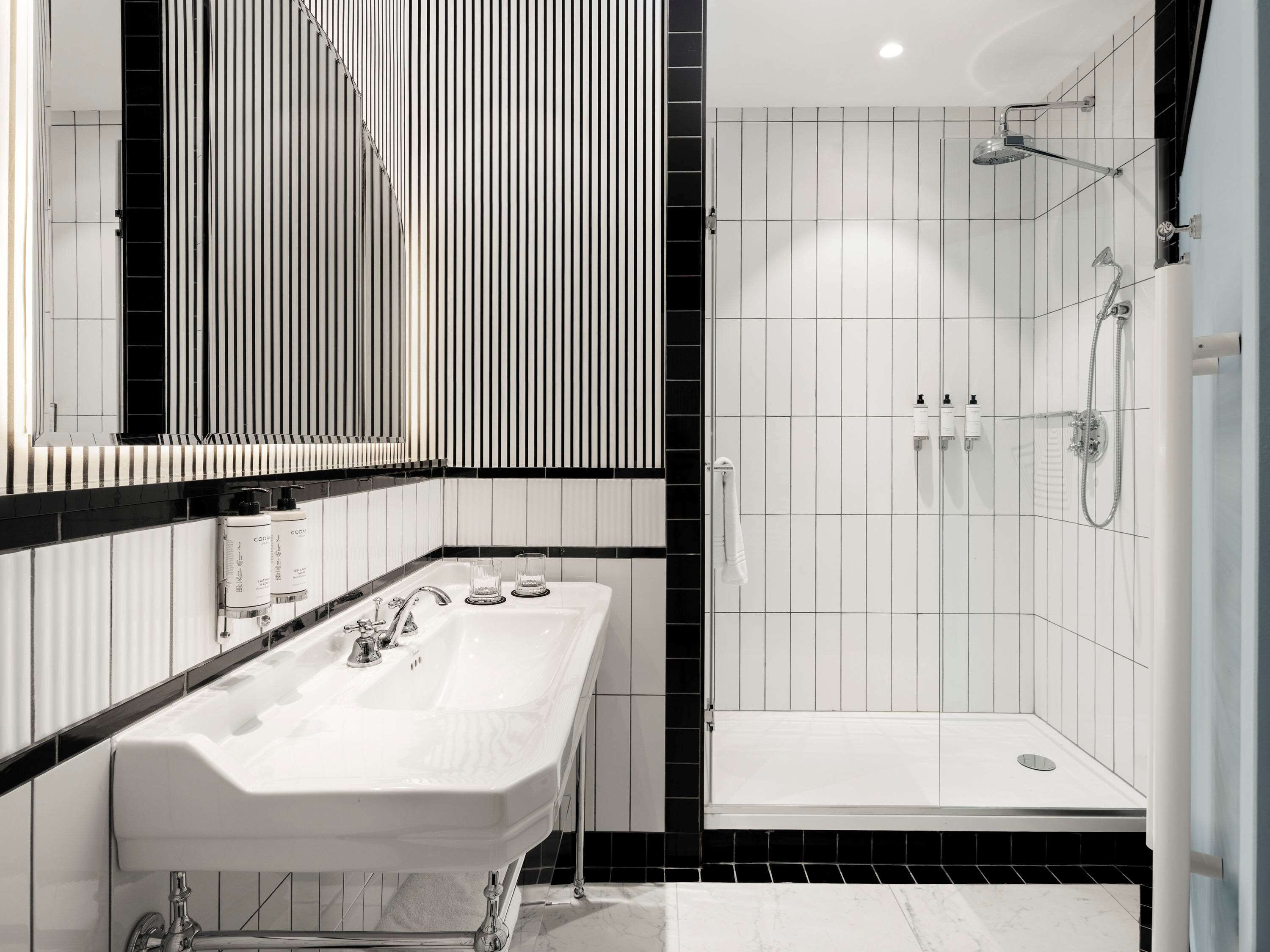 Ein modernes Badezimmer mit großem Spiegel, doppelter Waschbeckenanlage und barrierefreier Dusche.