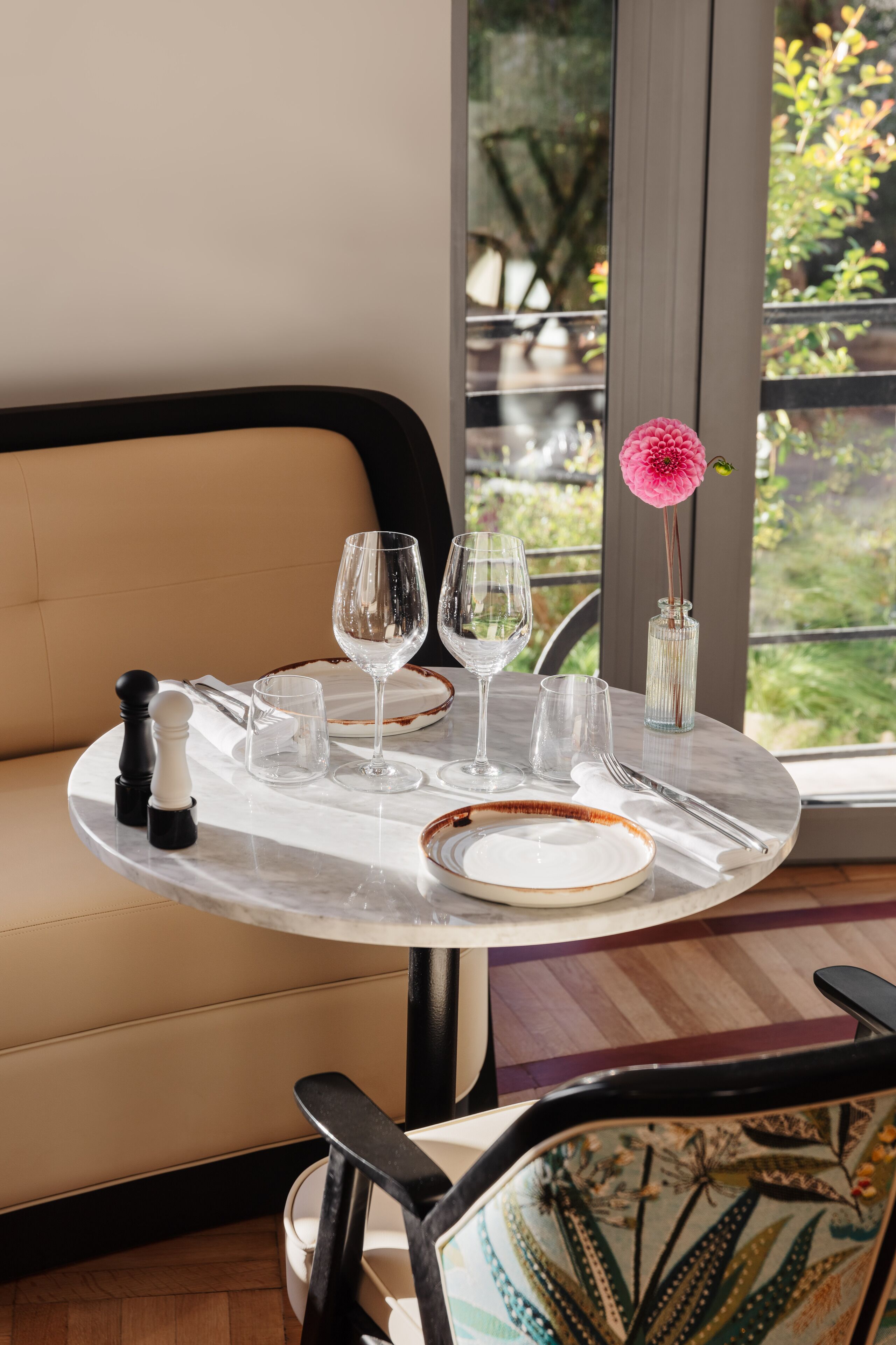 A dining table with a vase of pink flowers, salt and pepper shakers, and a set of cutlery.