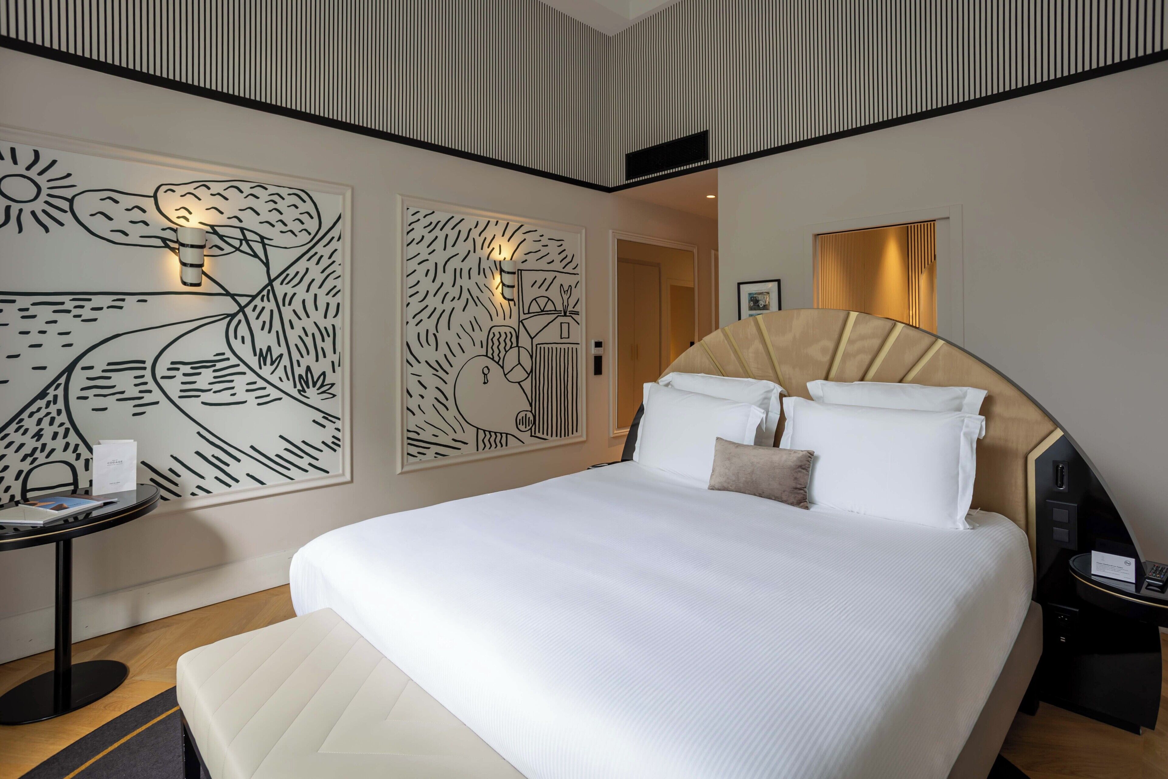 Een hotelkamer met een groot bed, nachtkastje, een kunstwerk aan de muur en een spiegel.