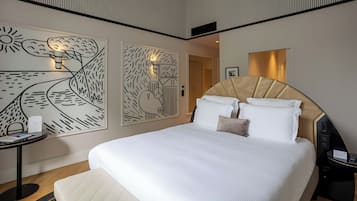 Een hotelkamer met een groot bed, nachtkastje, een kunstwerk aan de muur en een spiegel.