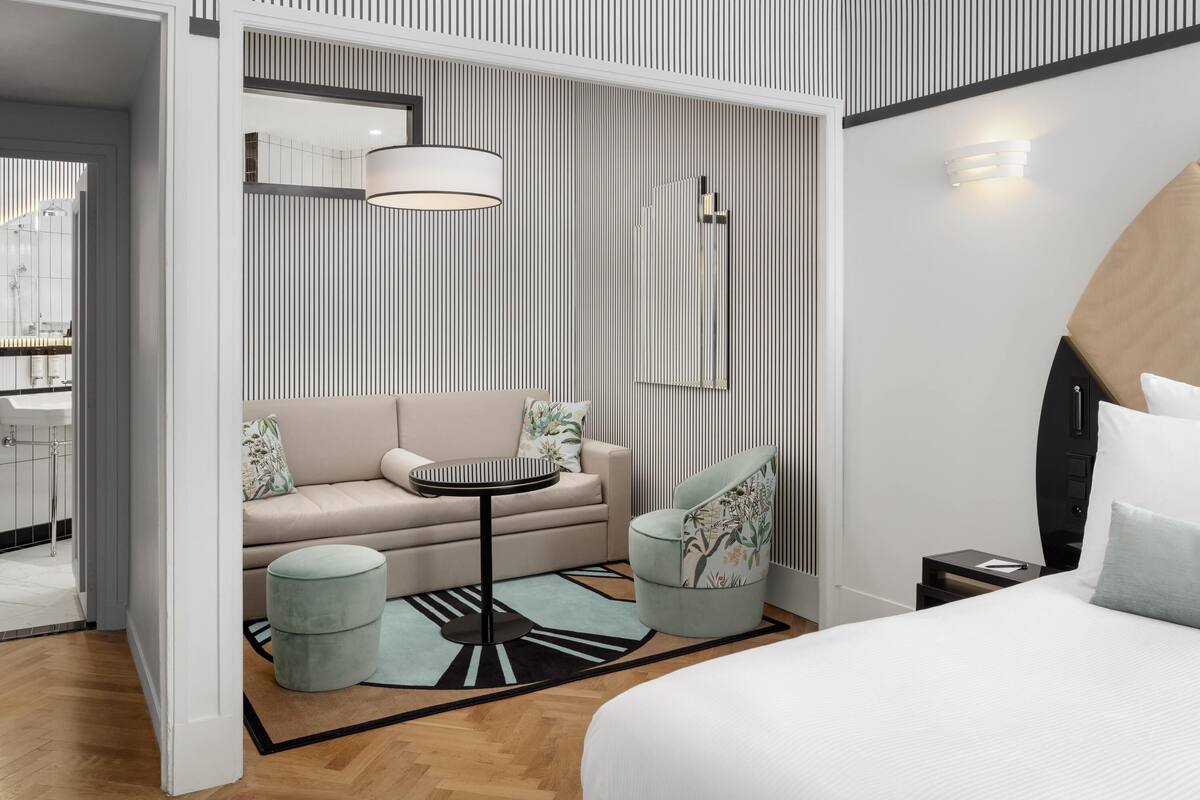 Ein modernes Hotelzimmer mit Bett, Sofa, rundem Tisch und einem kleinen Beistelltisch.