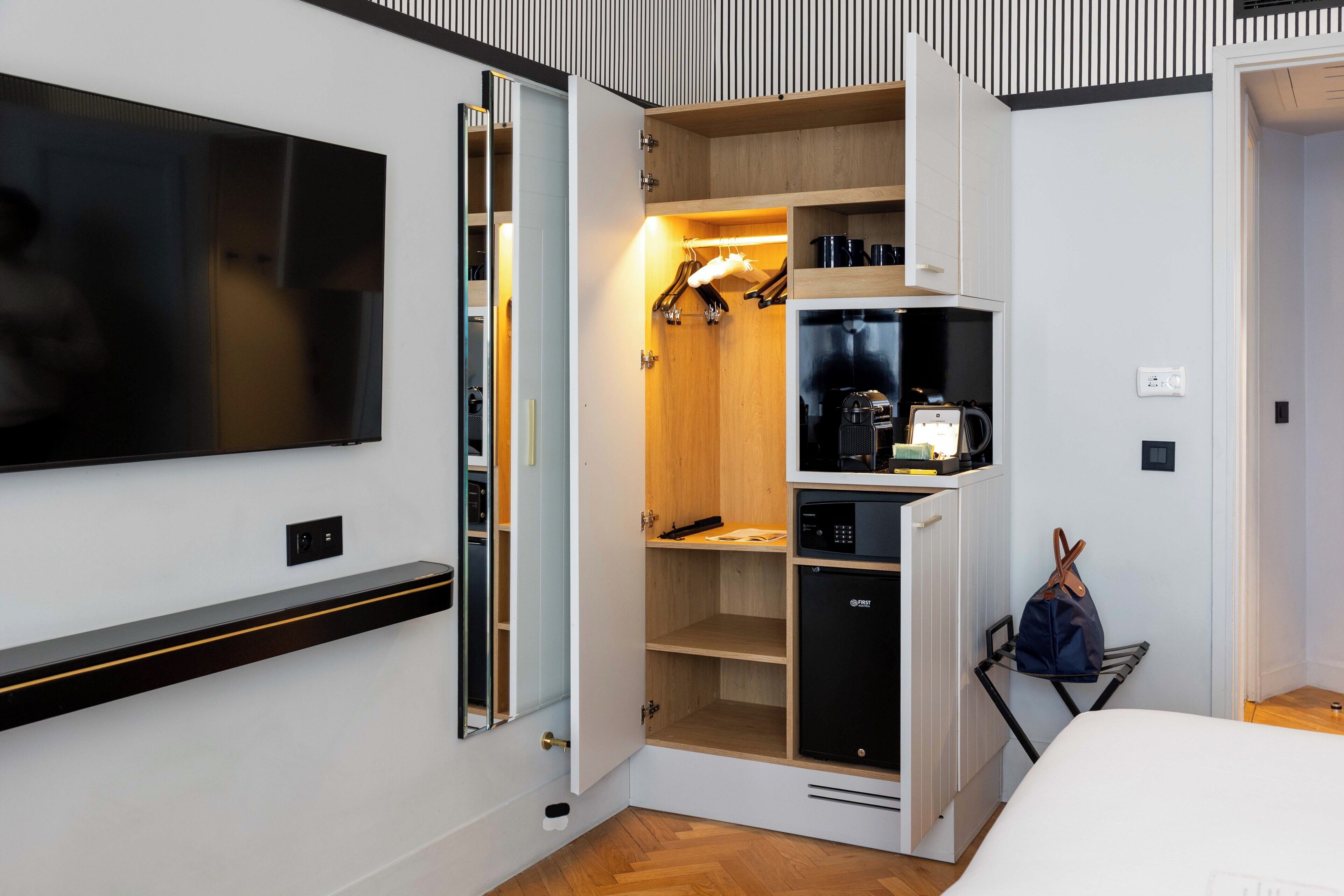 Habitación de hotel compacta con televisión, minibar, kitchenette pequeña y armario con espacio para colgar.