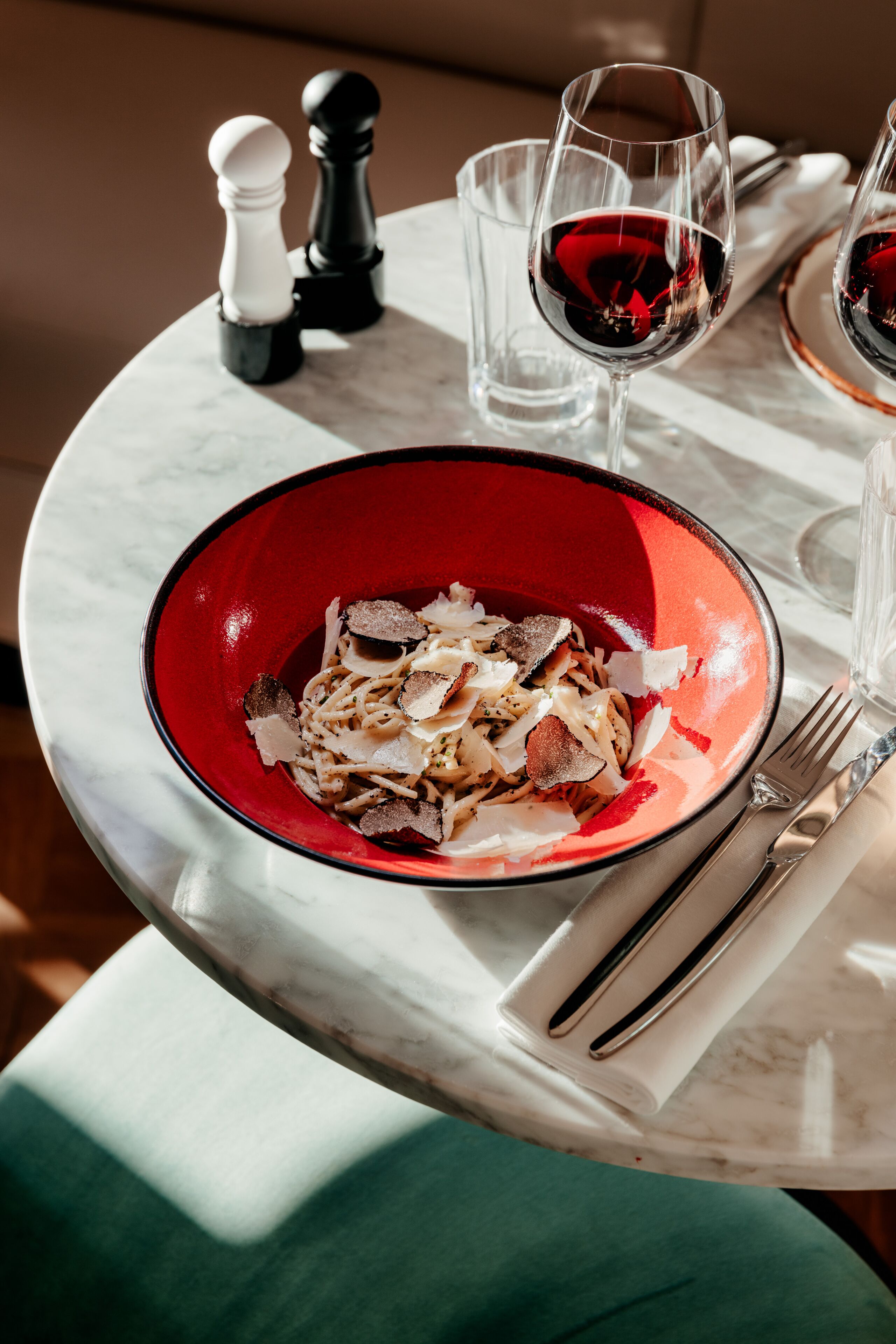 Une table à manger avec un saladier rouge rempli de pâtes, des verres à vin et des couverts.