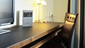 Habitación de hotel con un escritorio de madera, una silla, televisor, lámpara y un cuadro abstracto enmarcado en la pared.