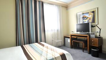 Habitación de hotel con cama, escritorio, computadora, televisor y una silla.