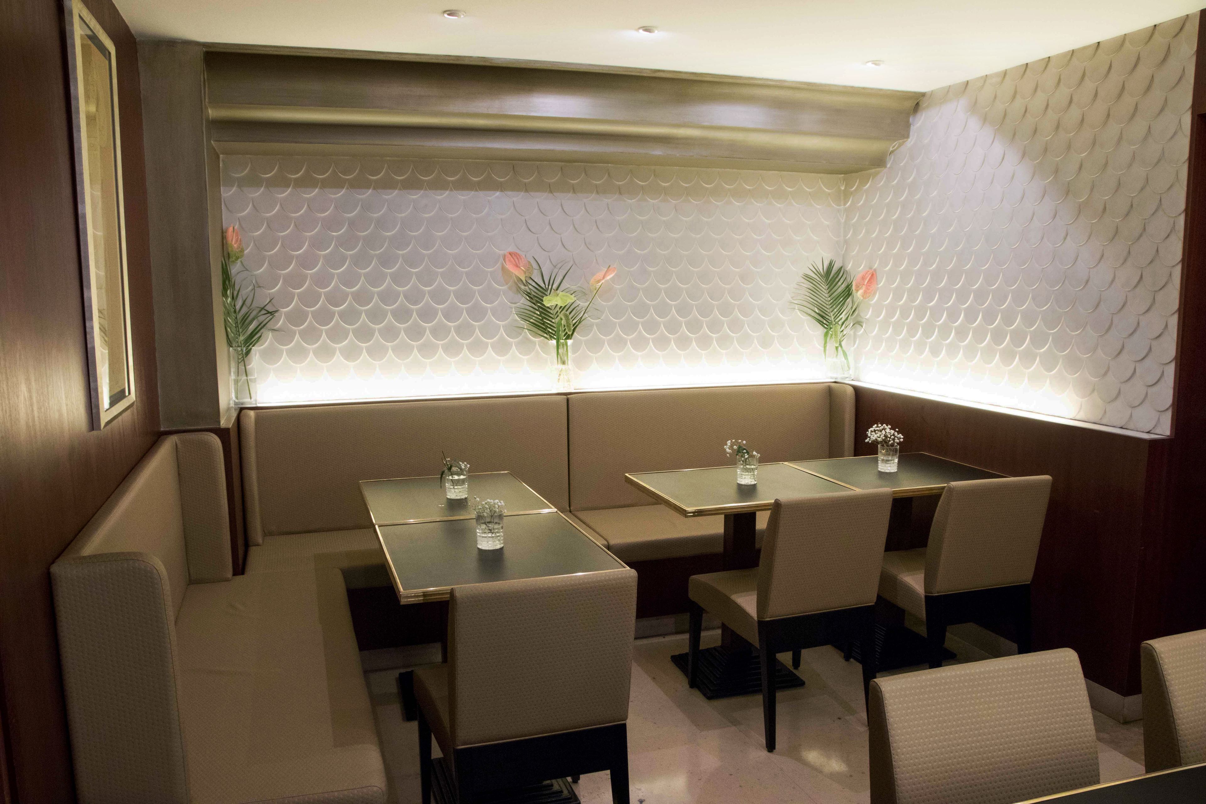 A restaurant with booth seating and tables, featuring a scalloped wall design and small floral centerpieces.