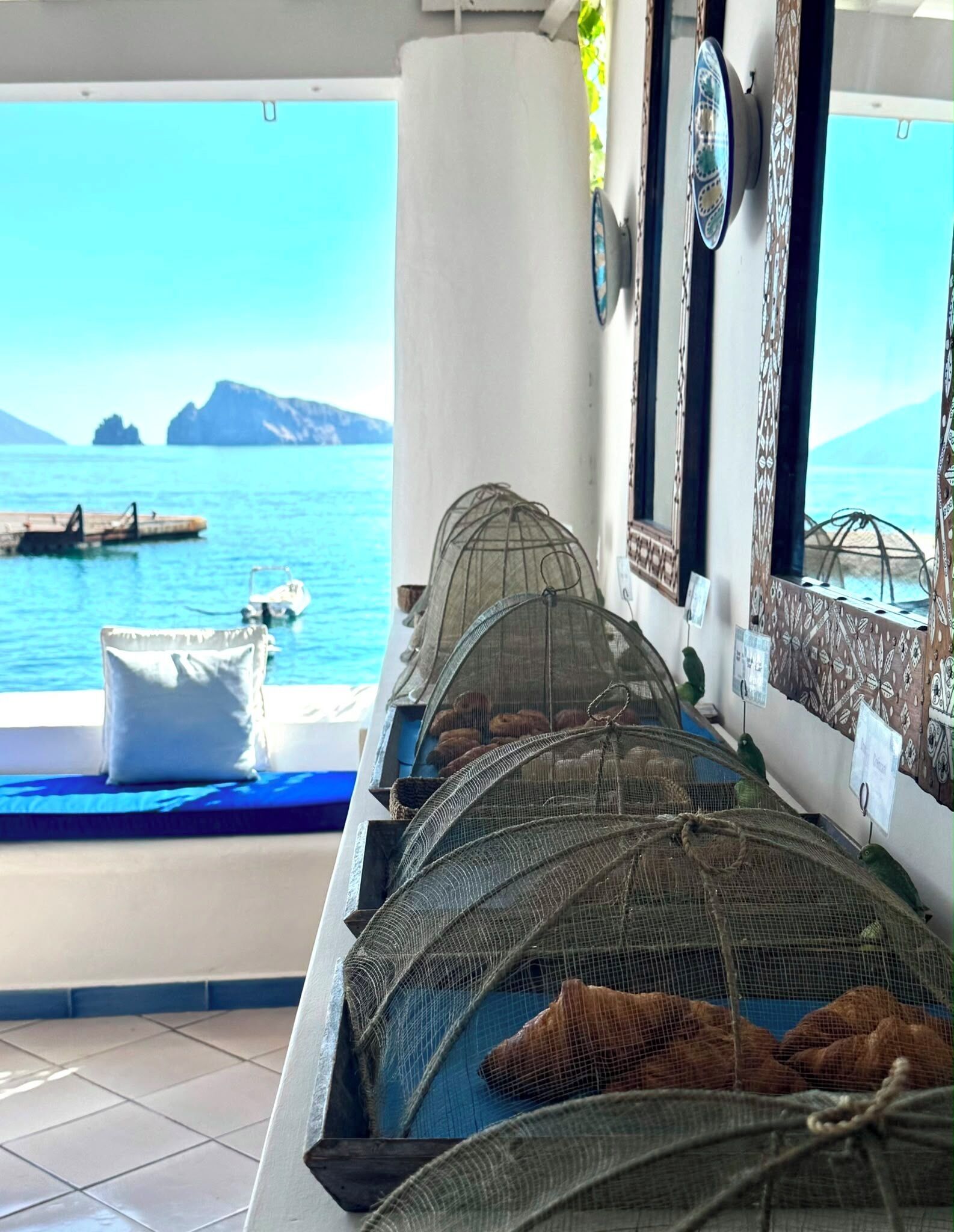A room with a view of the sea, a bed with a blue mattress, and a window with decorative elements.