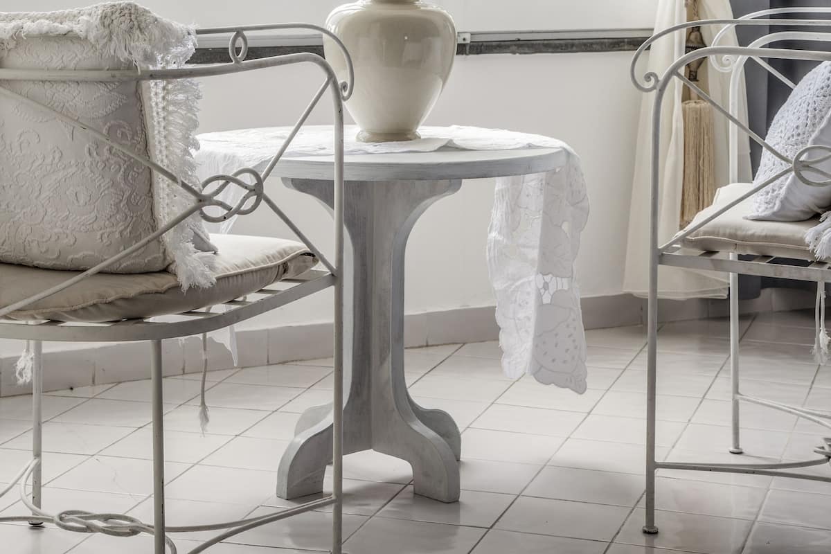 Ein Zimmer mit Fenster, einer weißen Vase auf einem Tisch und zwei Metallstühlen.